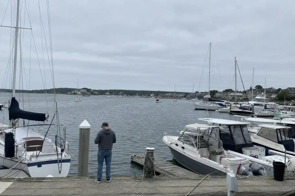 Segelbåtar förtöjda i en marina med öppet kustvatten i bakgrunden, där båtdelning utmanar på stormig marknad.
