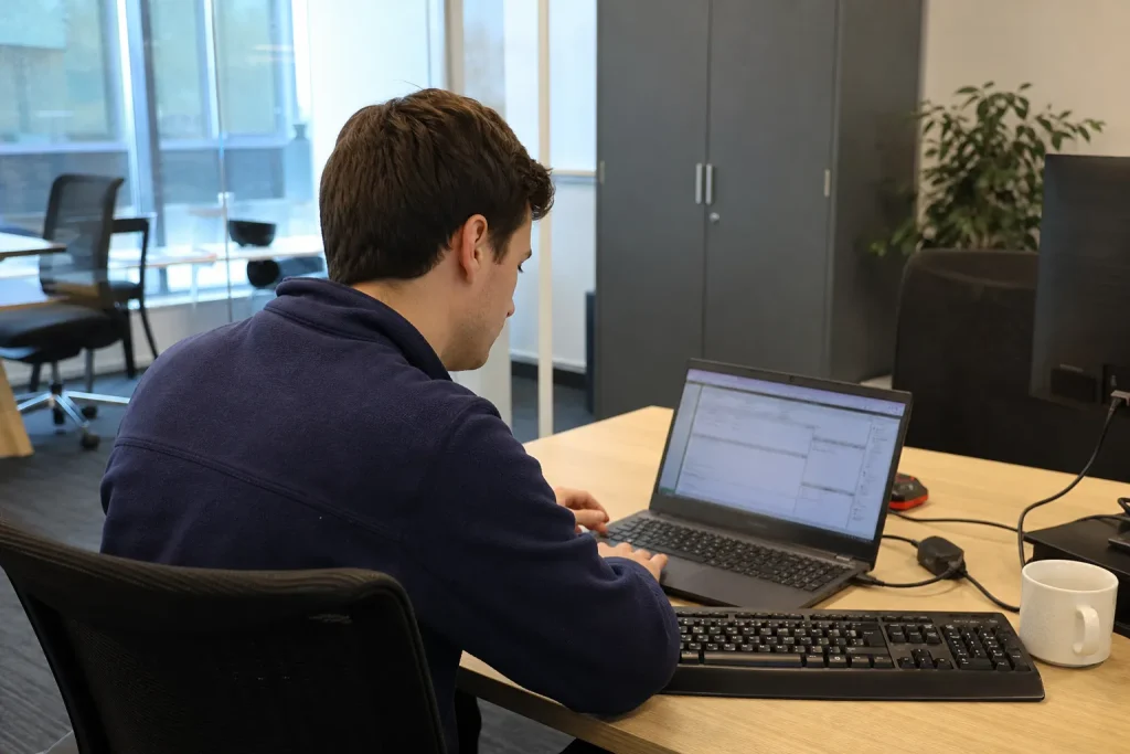 Person arbetar koncentrerat vid laptop på kontoret inom ramen för ISO 27001 certifiering.
