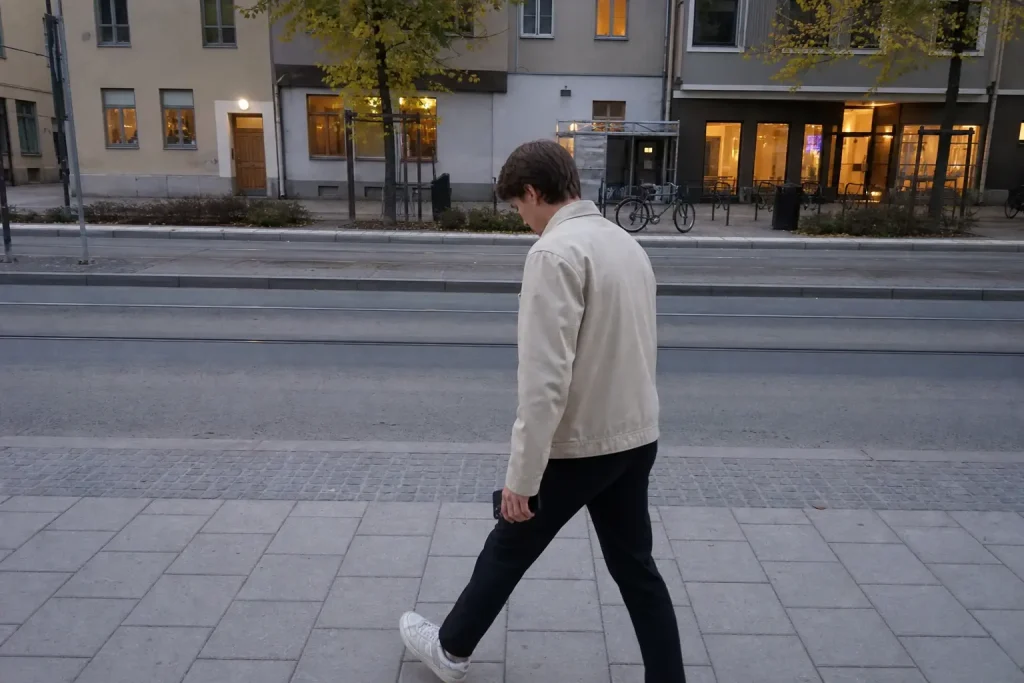 Person i lätt jacka går snabbt på gata i Stockholm nära spårvagnshållplats en tidig kväll.